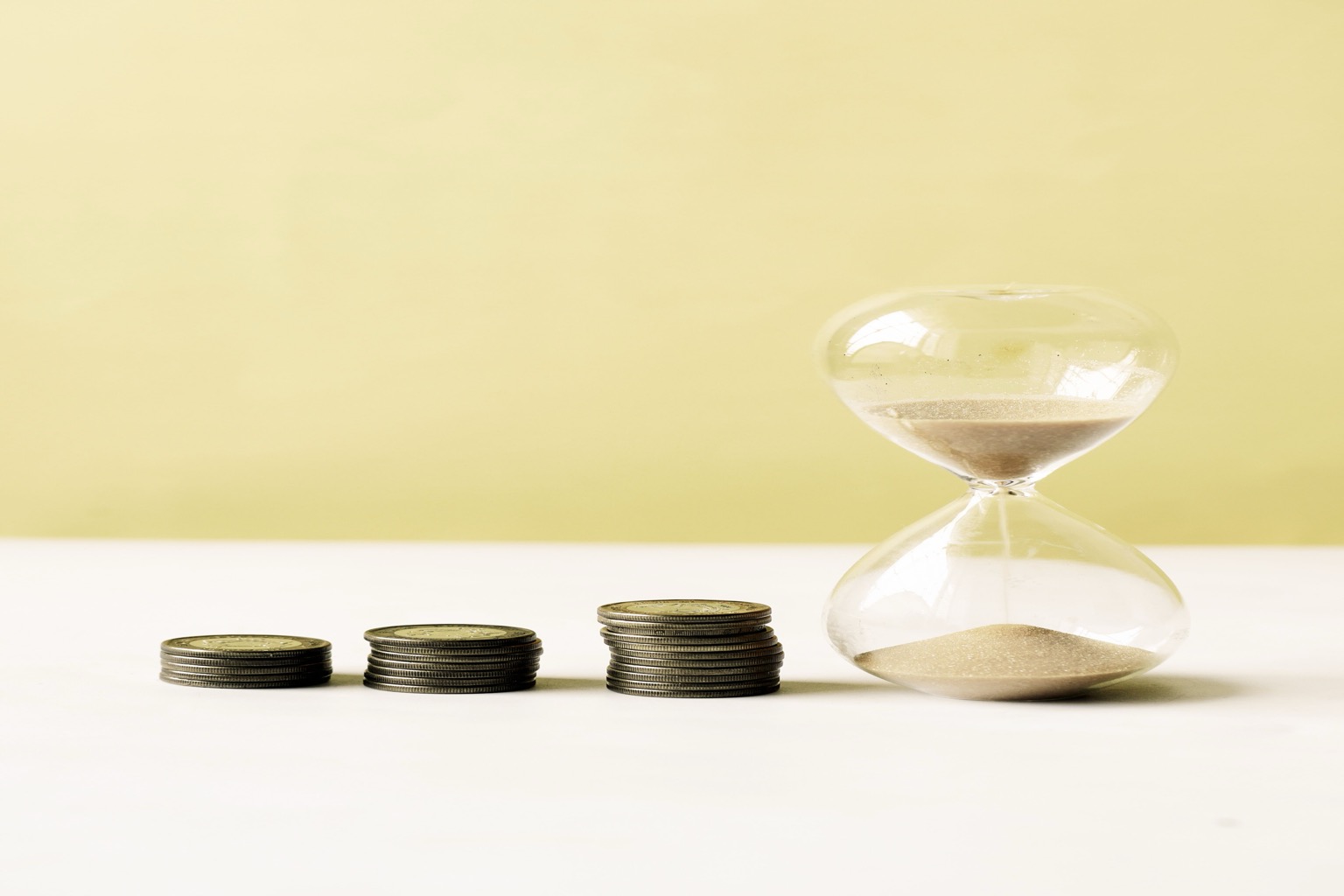 Symbolisches Stockfoto: Münzstapel und Sanduhr stehen für Geldwert und Zeit